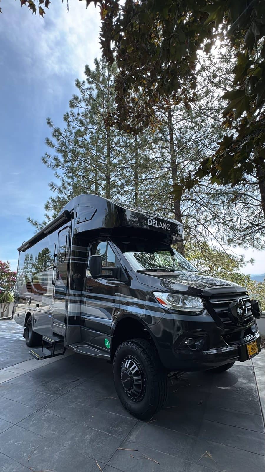 Dark grey adventure van detailed in a driveway among tall pines.