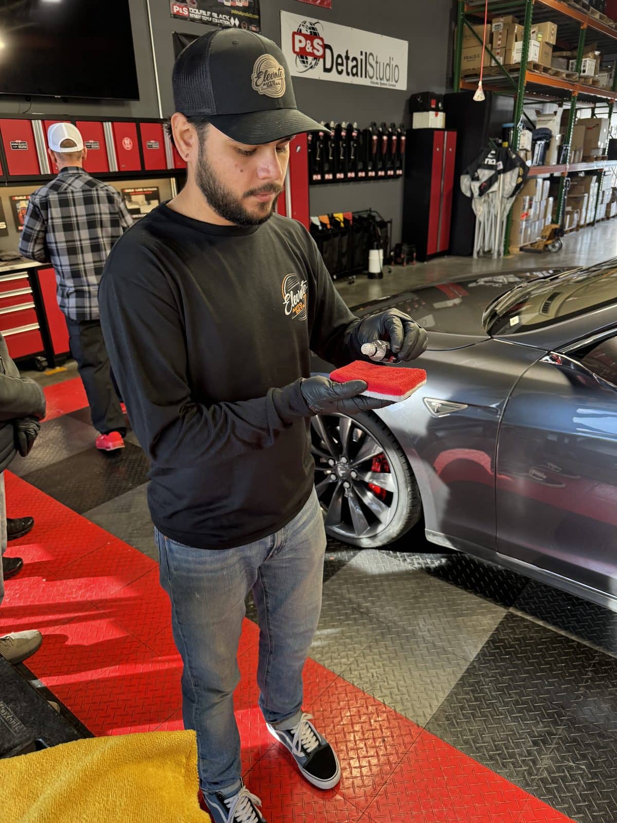 Detailer holding an applicator pad beside a car inside a detailing shop.